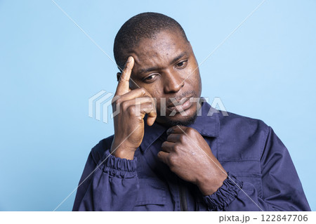 Male security officer is thinking about better protecting the mall area, finding new safety measures against blue background. Young pensive agent in uniform works on safeguarding duty. Male security officer is thinking about better protecting the mall area, finding new safety measures against blue background. Young pensive agent in uniform works on safeguarding duty. 122847706