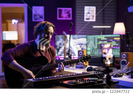 Musician teaching guitar lessons on internet with tutorials for social media pages, explaining strings accords on acoustic instrument. Guitarist doing online singing classes, filming with smartphone. Musician teaching guitar lessons on internet with tutorials for social media pages, explaining strings accords on acoustic instrument. Guitarist doing online singing classes, filming with smartphone. 122847722