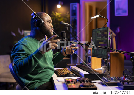 Young singer recording his new composed song on microphone, editing the tracks with mixing console and professional software. Artist manipulating sounds to create a good soundtrack. Young singer recording his new composed song on microphone, editing the tracks with mixing console and professional software. Artist manipulating sounds to create a good soundtrack. 122847796