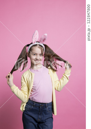 Optimistic little girl with fluffy ears and pigtails is enthusiastic about celebration of Easter, posing for the camera. Fabulous small kid on a pink background being joyful for the spring festivity. Optimistic little girl with fluffy ears and pigtails is enthusiastic about celebration of Easter, posing for the camera. Fabulous small kid on a pink background being joyful for the spring festivity. 122847800