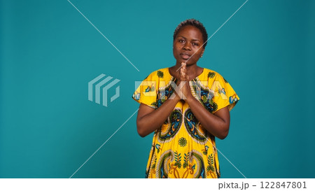 Confident optimistic woman holding hands in a prayer and talks to Jesus, praying for good luck and health against blue background. Young adult with spiritual belief being religious. Camera B. 122847801