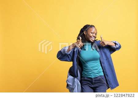 Woman doing thumbs up hand gesturing, showing approval, having positive mood. Cheerful BIPOC person presenting confirmation, doing agreement finger sign, studio background 122847822