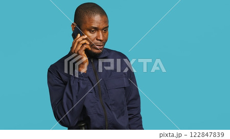 Portrait of security guard at work using phone to make call to friends while overseeing premises. Private law enforcement worker in telephone call with mates, studio backdrop, camera A Portrait of security guard at work using phone to make call to friends while overseeing premises. Private law enforcement worker in telephone call with mates, studio backdrop, camera A 122847839