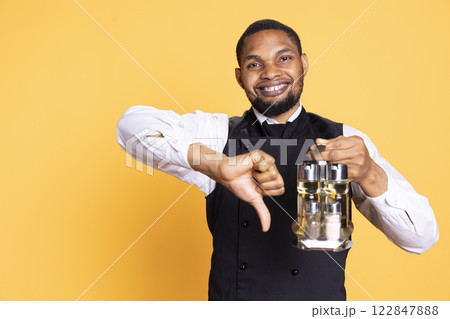 Professional butler presenting a thumbs down sign on camera, showing his disagreement and negative emotions in studio. Catering worker gives a dislike symbol, customer service. 122847888