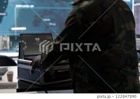 Military specialist monitors satellite data real time information on laptop, coordinates strategic operations to support decision making and national protocols in a high tech control room. Military specialist monitors satellite data real time information on laptop, coordinates strategic operations to support decision making and national protocols in a high tech control room. 122847890