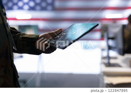 Professionals in US military uniforms operate computers and big screen, working on surveillance and intelligence to ensure national security from a high tech control center. Close up. 122847895