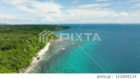 Beautiful sandy beach on a tropical island with abundant green trees along with a small rock formation in the shore. Beautiful sandy beach on a tropical island with abundant green trees along with a small rock formation in the shore. 122848114