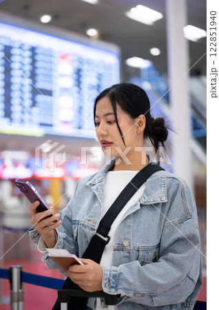 A positive Asian female passenger checks her boarding time on her phone, standing in the airport 122851940