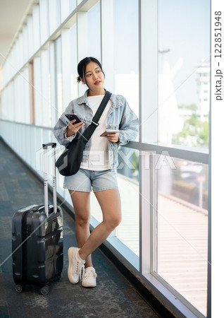 A confident Asian woman gazing at the airport runway while waiting for her flight. 122851948