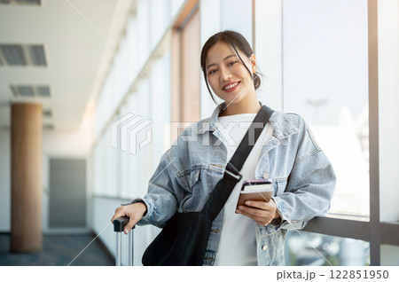 An attractive Asian female passenger stands in the airport terminal with a luggage beside her. 122851950