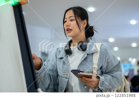 A focused Asian female passenger is checking in for her flight at an airport self-check-in kiosk. A focused Asian female passenger is checking in for her flight at an airport self-check-in kiosk. 122851988