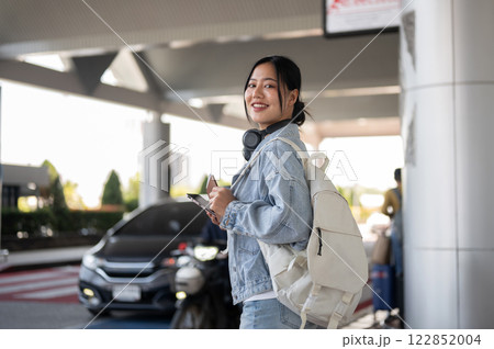 A beautiful Asian female traveler stands at an airport pickup point, waiting for a taxi. 122852004