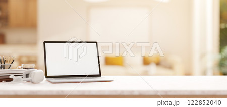 A laptop and stationery on a white desk with a blurred background of a modern bright living room. 122852040