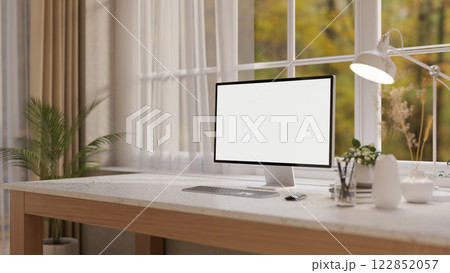 A computer and decorative items on a white marble desk, set against a window in a minimalist room. 122852057