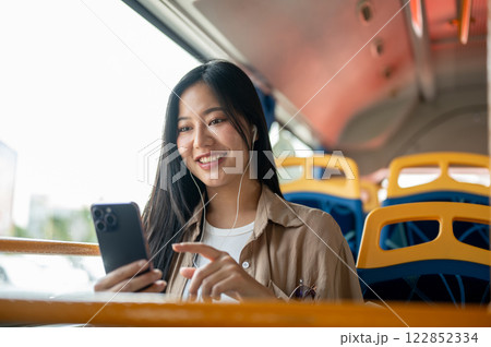 A beautiful Asian woman enjoys chatting on her smartphone while on a bus, commuting in the city. 122852334