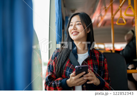 A beautiful Asian woman travels by public bus in the city, sitting by the window. A beautiful Asian woman travels by public bus in the city, sitting by the window. 122852343