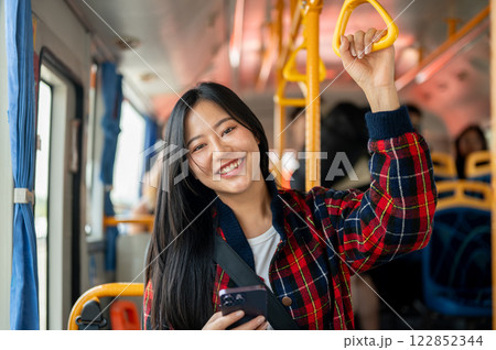 A smiling Asian female college student holds a handrail while riding a bus to college in the morning A smiling Asian female college student holds a handrail while riding a bus to college in the morning 122852344