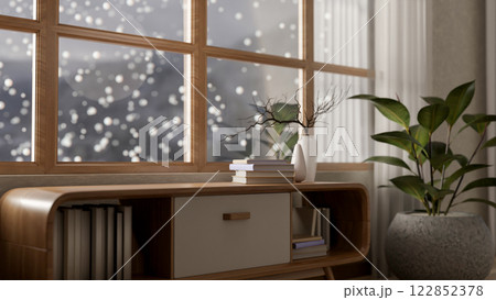 A minimalist wooden cabinet and a houseplant placed by a window overlooking a snowy winter view. 122852378