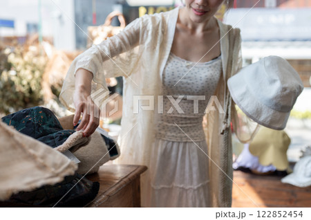 A close-up of an Asian woman carefully selecting items in a hat shop, enjoying her shopping spree. 122852454