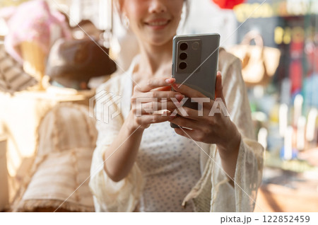 A close-up of a happy Asian customer is taking a picture of items in a hat shop, enjoying shopping. 122852459