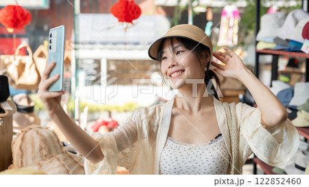A cheerful Asian-Chinese female customer enjoys blogging on her smartphone while shopping. A cheerful Asian-Chinese female customer enjoys blogging on her smartphone while shopping. 122852460