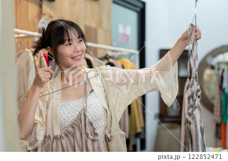 A happy Asian female customer is selecting items to buy in a clothing store, enjoying shopping alone 122852471