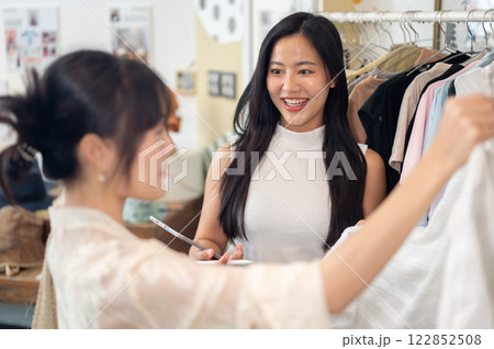 A friendly and service-minded Asian female clothing store employee is talking to a customer. A friendly and service-minded Asian female clothing store employee is talking to a customer. 122852508