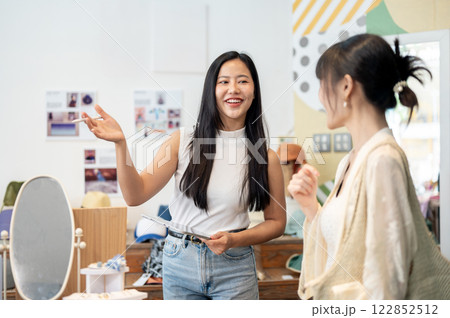 A service-minded Asian female clothing store owner is talking to a customer, working in her shop. A service-minded Asian female clothing store owner is talking to a customer, working in her shop. 122852512