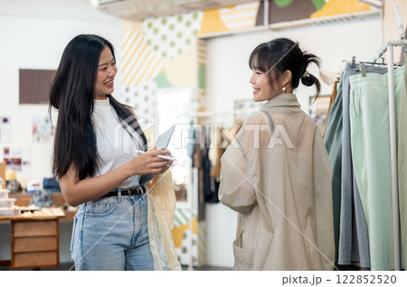 A service-minded and friendly female clothing store employee is helping a customer select an item. A service-minded and friendly female clothing store employee is helping a customer select an item. 122852520