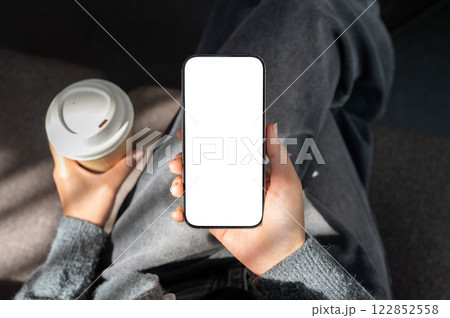 A close-up top view of a woman sitting in a coffee shop, uses her smartphone and sips her coffee. 122852558