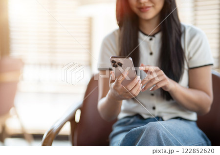 A beautiful Asian woman enjoys chatting on her smartphone while relaxing in a coffee shop. A beautiful Asian woman enjoys chatting on her smartphone while relaxing in a coffee shop. 122852620