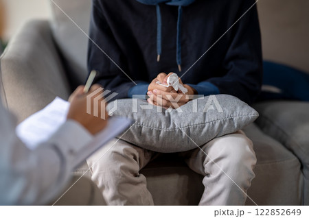 A stressed man sitting on a sofa, clasping his hands together during a mental health checkup. A stressed man sitting on a sofa, clasping his hands together during a mental health checkup. 122852649