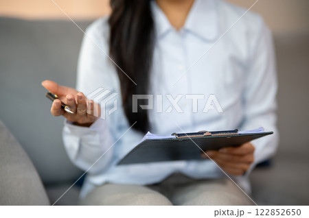 A close-up of a female psychologist holding a medical clipboard and a pen while talking to a patient 122852650
