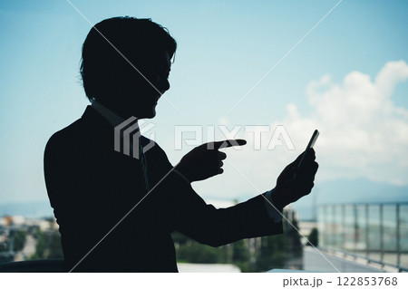 スマホを操作する男性のシルエット（特殊詐欺・誹謗中傷） 122853768