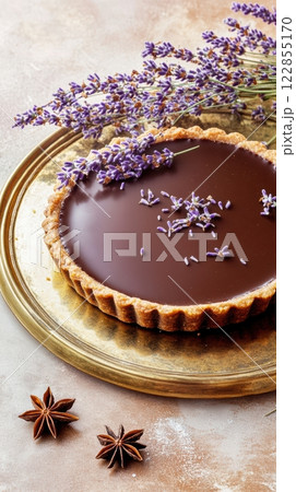 Chocolate tart garnished with lavender blossoms resting on golden platter, complemented by star anise, presenting delicate culinary artistry 122855170