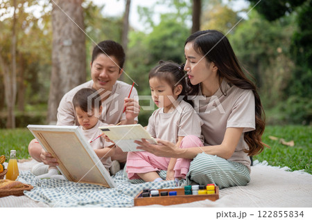 Lovely Asian parents take their kids on a picnic in a park, enjoying painting on a canvas together. Lovely Asian parents take their kids on a picnic in a park, enjoying painting on a canvas together. 122855834