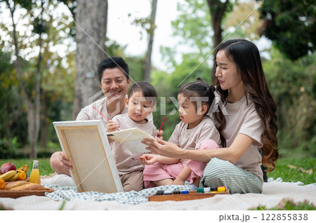 A happy Asian family enjoys painting on a canvas during a picnic in a public park. 122855838