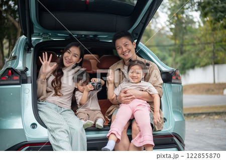 A happy and cheerful Asian family sitting in the trunk of their car, smiling at the camera. 122855870