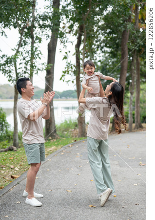 A cheerful little Asian boy smiles widely as his mom lifts him into the air, enjoying a joyful time. 122856206
