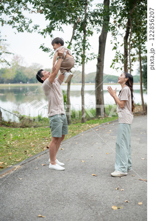 A cheerful little Asian boy smiles widely as his dad lifts him into the air, enjoying a joyful time. A cheerful little Asian boy smiles widely as his dad lifts him into the air, enjoying a joyful time. 122856207