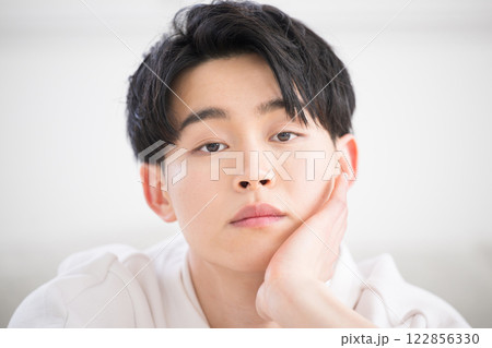 顎に手を当てて考える、頬杖などの悩むポーズの20代男性の美容やビューティーのイメージ　カメラ目線 122856330