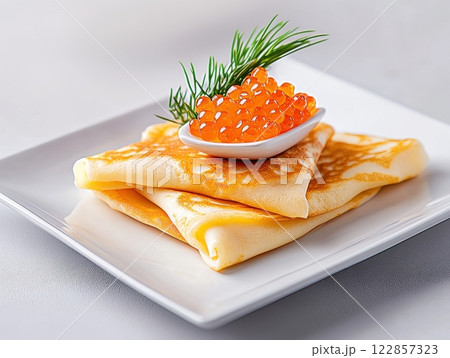 A close-up of thin folded pancakes on a square white plate, topped with a small dish of red caviar and garnished with fresh dill.  122857323