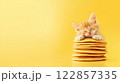 A sleepy kitten with soft orange fur gently rests its paws on a stack of pancakes, creating a peaceful and adorable scene. The yellow background adds to the warmth and calmness of the shot. 122857335