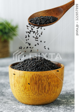 black sesame seeds falling from spoon in bowl on table 122857899