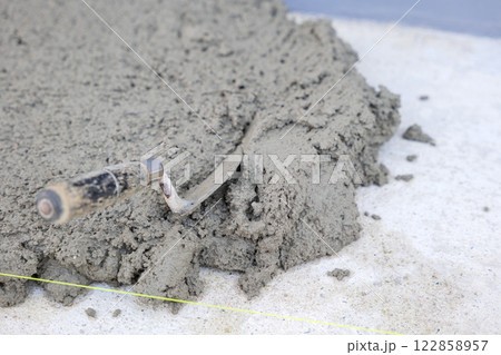 A trowel placed on gray concrete, surrounded by pull tabs and wedges, demonstrating tools and techniques in the process of laying tiles with a leveling system. A trowel placed on gray concrete, surrounded by pull tabs and wedges, demonstrating tools and techniques in the process of laying tiles with a leveling system. 122858957