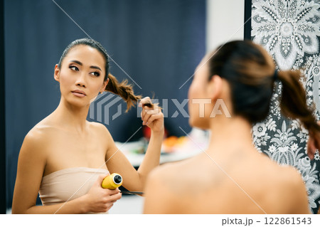 Beautiful asian woman fixing her hair looking in mirror. 122861543