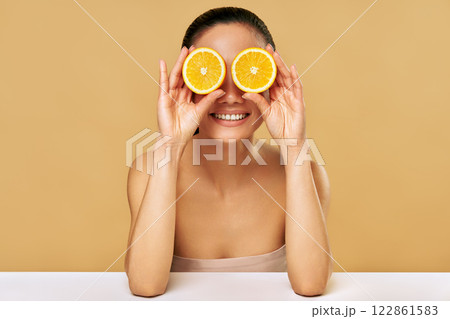 Playful positive asian woman covers eyes with two orange making funny faces 122861583