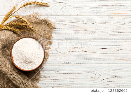 Flat lay of Wheat flour in wooden bowl with wheat spikelets on colored background. world wheat crisis Flat lay of Wheat flour in wooden bowl with wheat spikelets on colored background. world wheat crisis 122862663