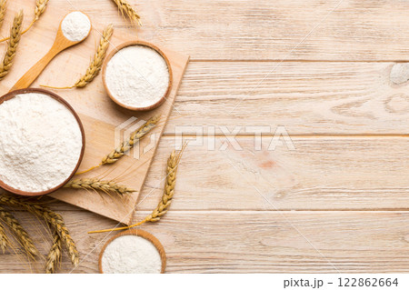 Flat lay of Wheat flour in wooden bowl with wheat spikelets on colored background. world wheat crisis Flat lay of Wheat flour in wooden bowl with wheat spikelets on colored background. world wheat crisis 122862664