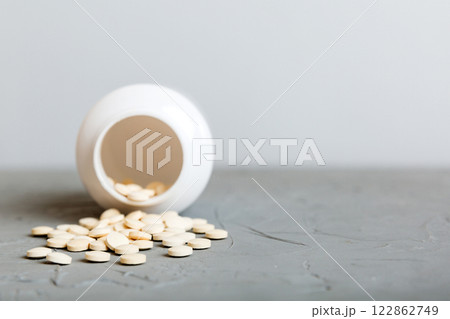 Medicine bottle and white pills spilled on a light background. Medicines and prescription pills flat lay background. White medical pills and tablets spilling out of a drug bottle 122862749
